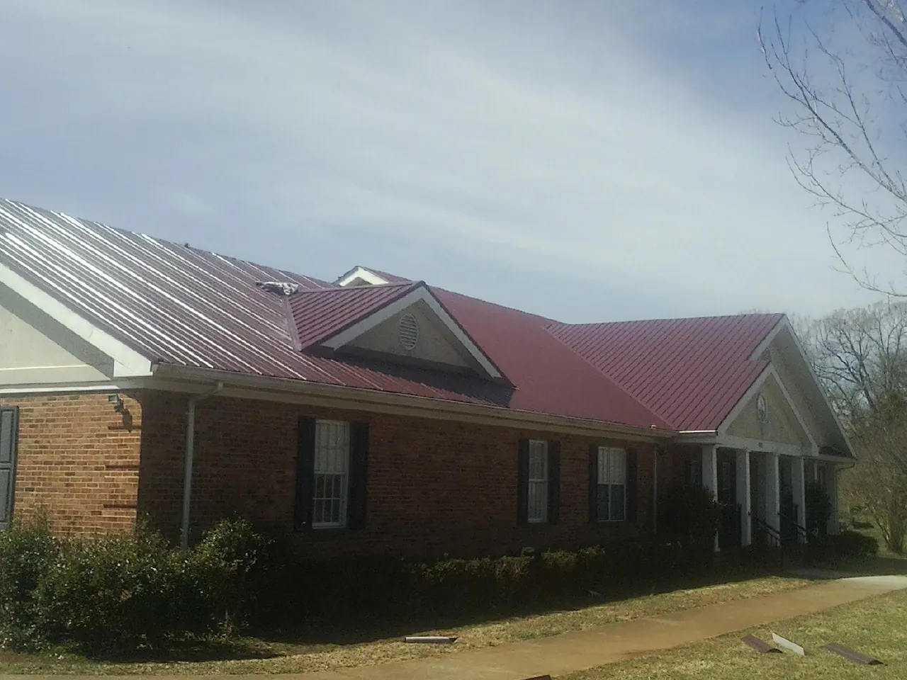 Red metal roof with gabled entries on a long brick building, from a Hail Damage Roof Repair job in Carleton
