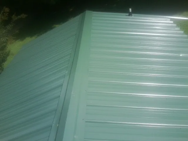 New green metal panels meeting at the ridge of a roof — Flat Roof Repair work by our crew in Carleton