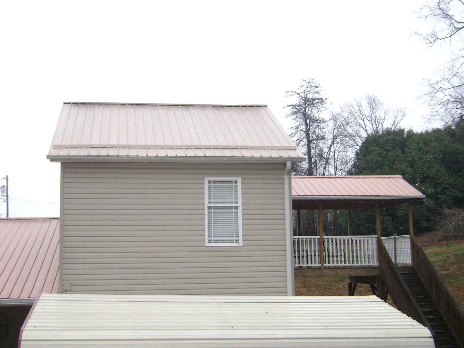 Tan metal roofs on a two story addition and attached porch, from a Roof Replacement job in Carleton
